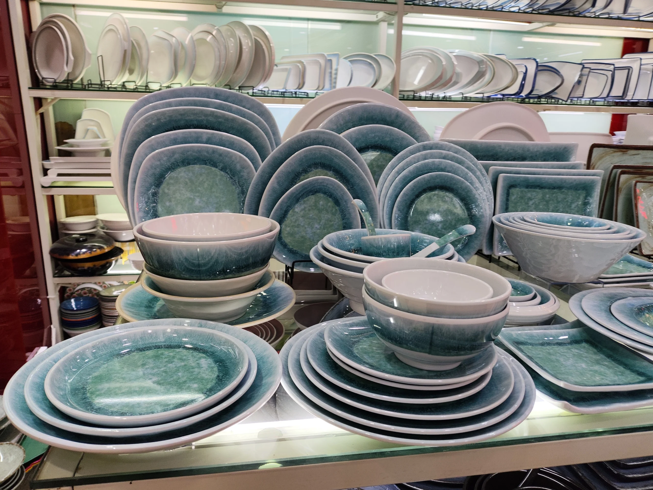 Plates and bowls in blue-green finishes displayed in a kitchenware showroom for sourcing