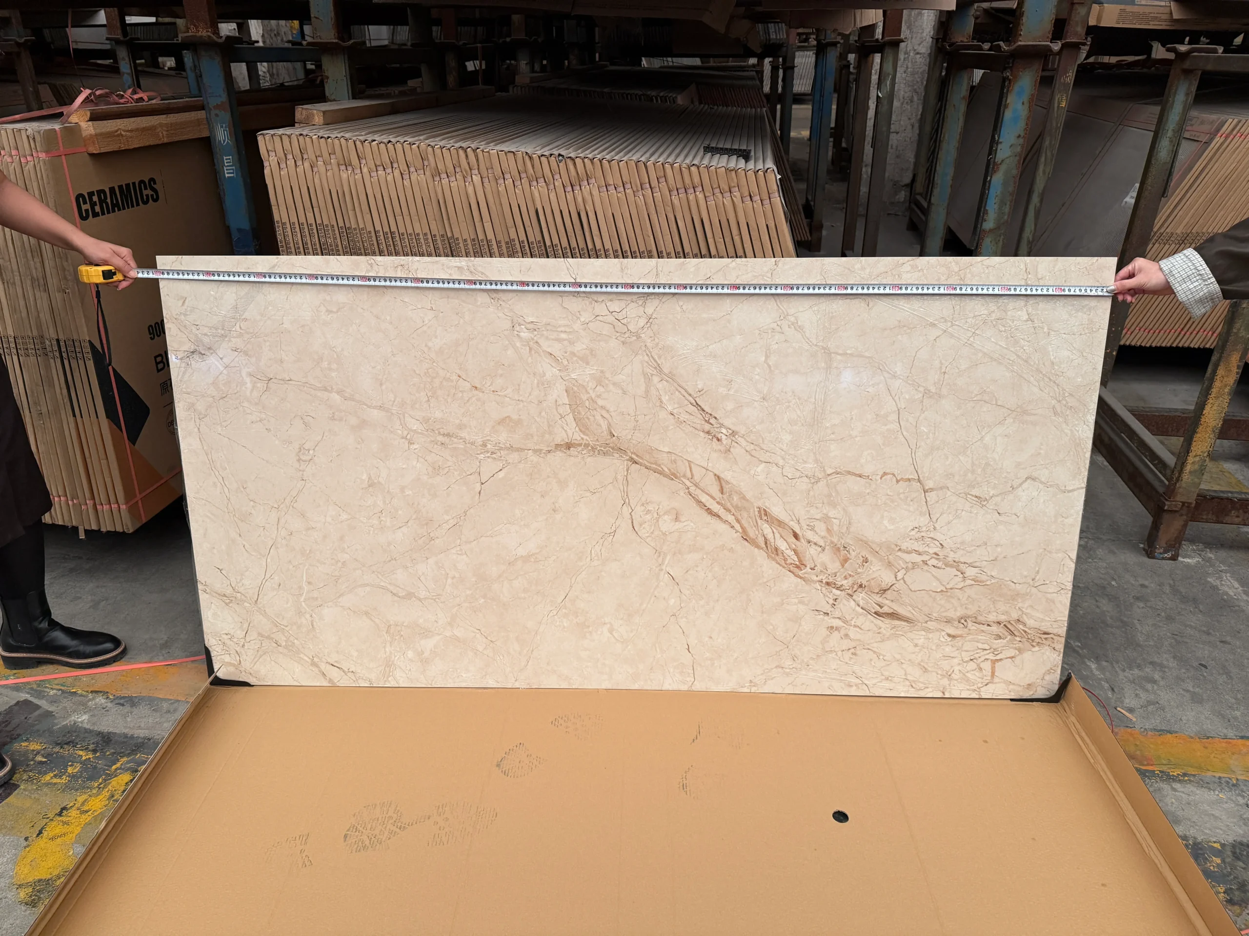 Tile Quality Control in China: How to Check Shade, Caliber, Flatness, Water Absorption and Packing 4 Workers measuring the width of a large beige marble-look tile with a tape measure at a tile warehouse in China.