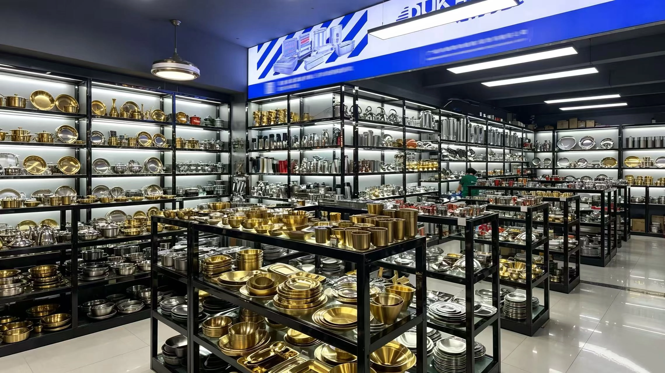 Metal kitchenware, bowls, plates and serving trays in silver and gold finishes displayed in a showroom